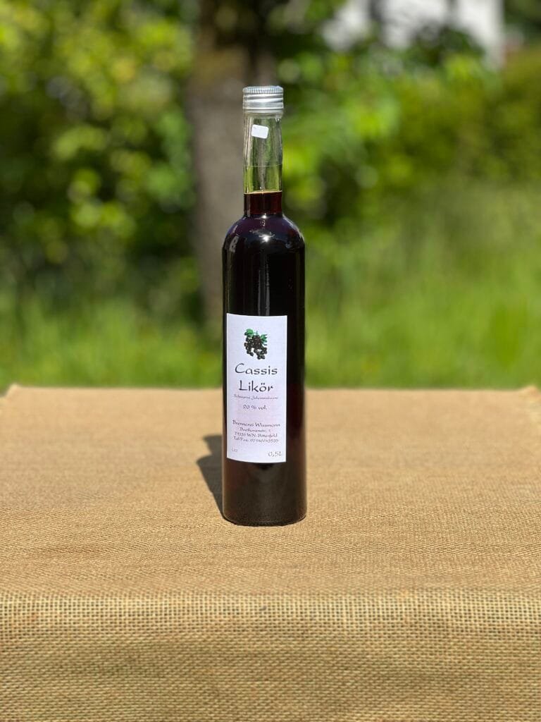 Eine Flasche Cassis-Likör auf einem Tisch mit idyllischem grünen Hintergrund.