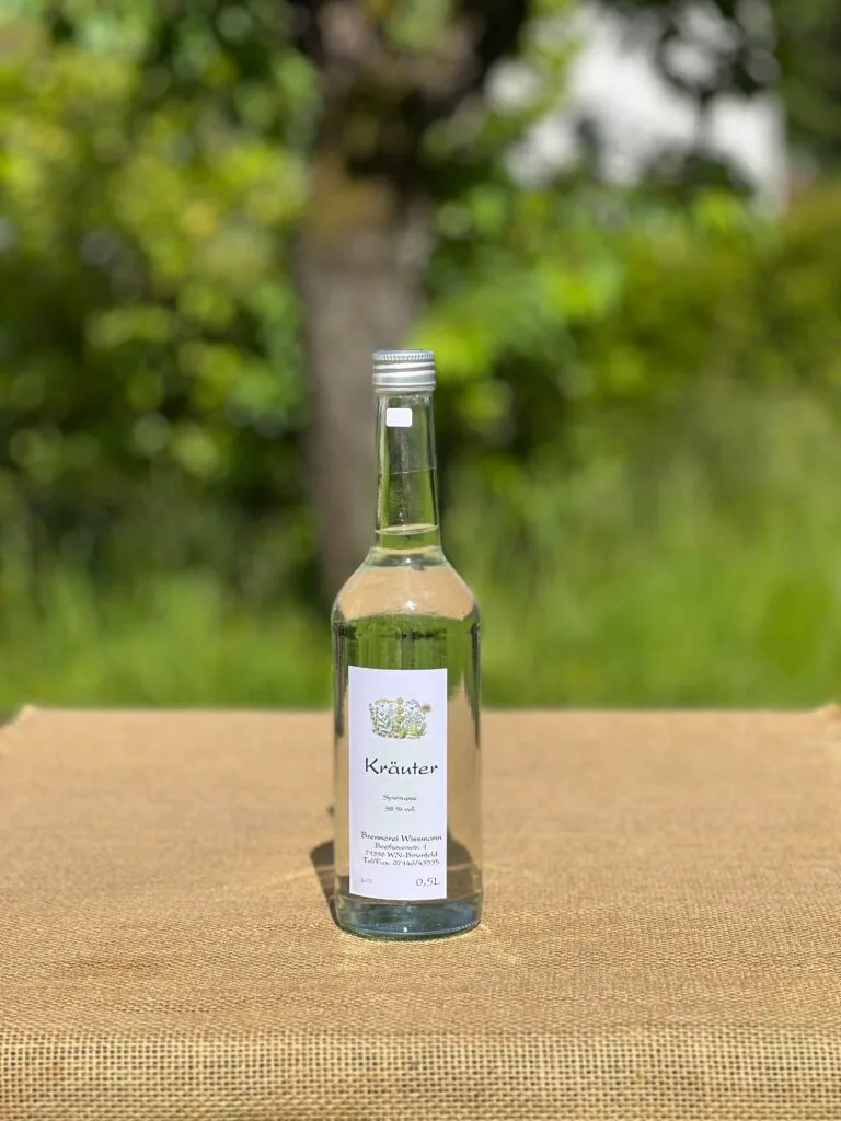 Eine Flasche Kräuterbrand auf einem Tisch mit idyllischem grünen Hintergrund.