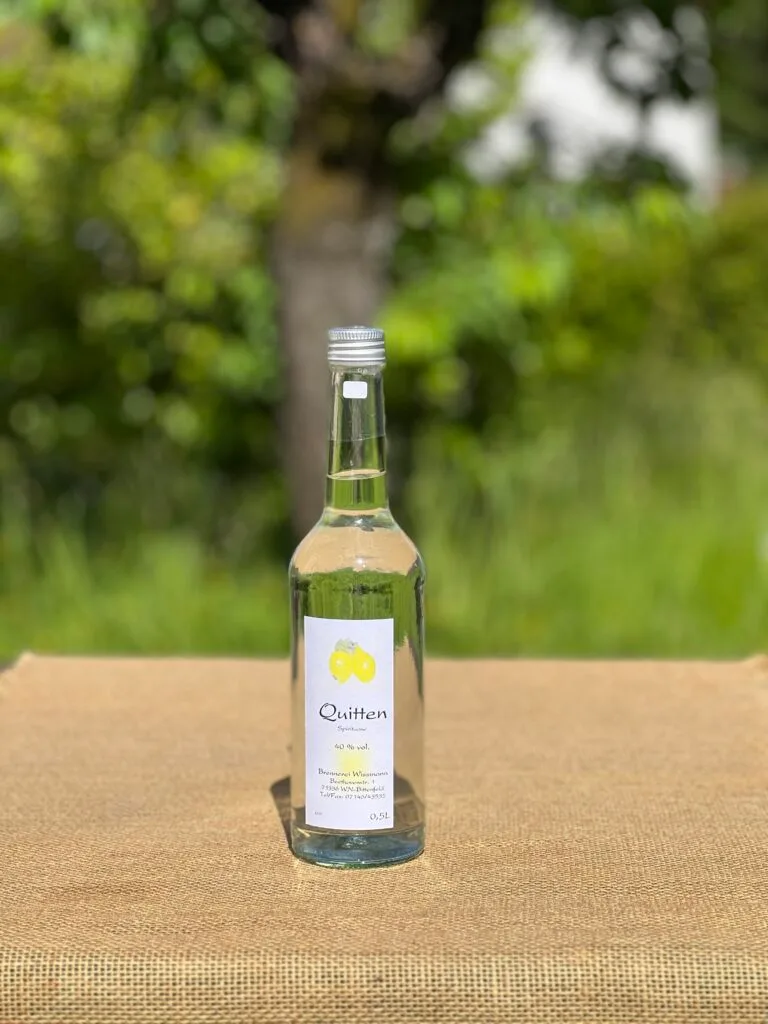 Eine Flasche Quittengeist auf einem Tisch mit idyllischem grünen Hintergrund.