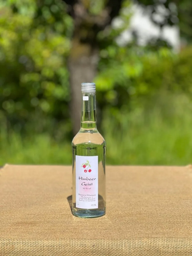 Eine Flasche Himbeergeist auf einem Tisch mit idyllischem grünen Hintergrund.