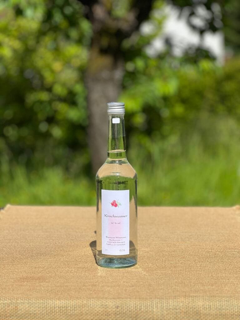 Eine Flasche Kirschwasser auf einem Tisch mit idyllischem grünen Hintergrund.