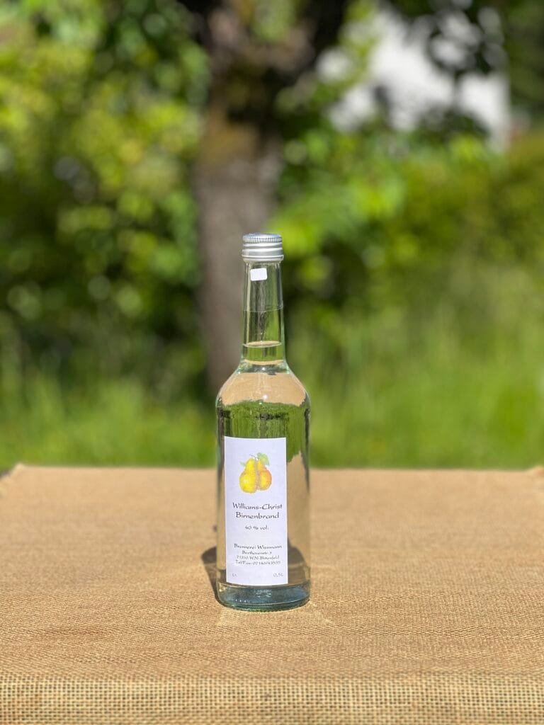 Eine Flasche Williams-Christ- Birnenbrand auf einem Tisch mit idyllischem grünen Hintergrund.