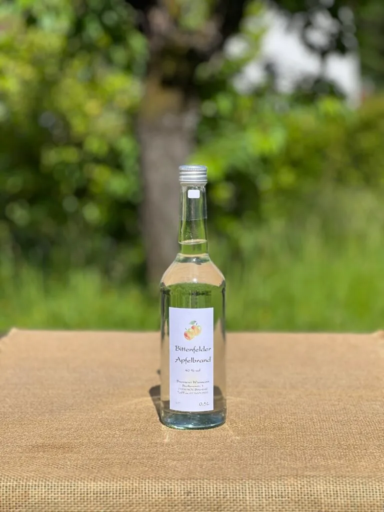 Eine Flasche Apfelbrand auf einem Tisch mit idyllischem grünen Hintergrund.