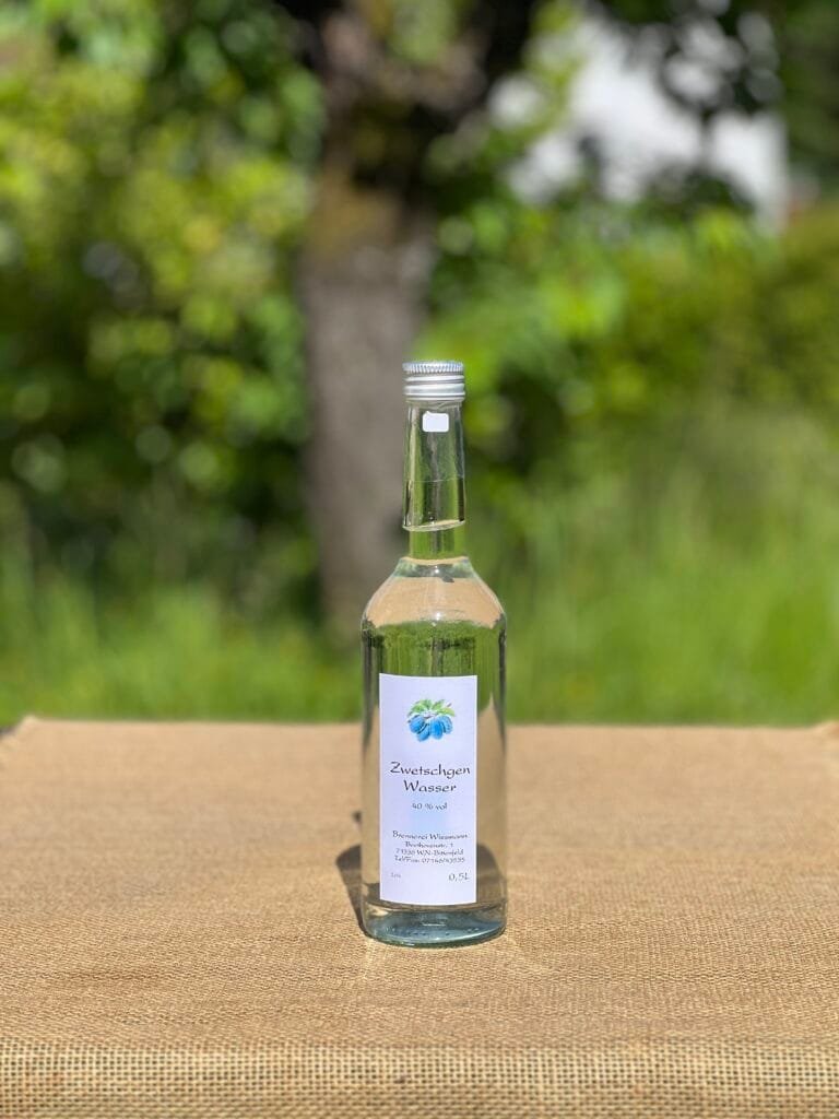 Eine Flasche Zwetschgenwasser auf einem Tisch mit idyllischem grünen Hintergrund.