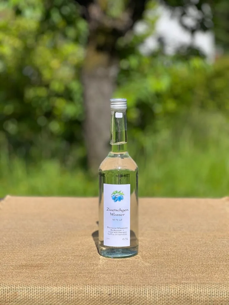Eine Flasche Zwetschgenwasser auf einem Tisch mit idyllischem grünen Hintergrund.