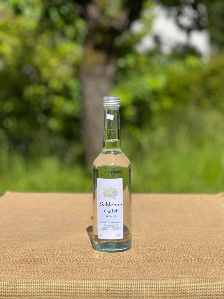 Eine Flasche Schlehengeist auf einem Tisch mit idyllischem grünen Hintergrund.