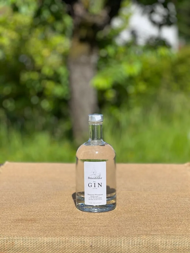 Eine Flasche Bittenfelder Gin auf einem Tisch mit idyllischem grünen Hintergrund.
